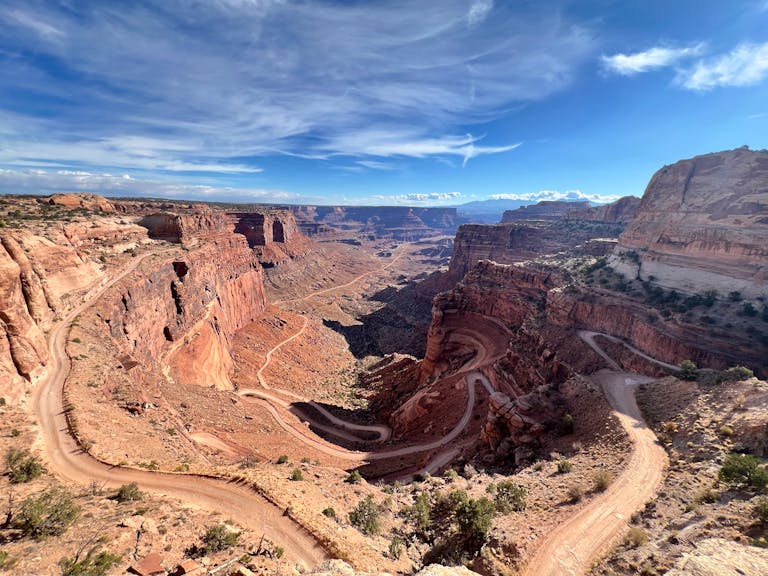 A breathtaking view of a red rock canyon with a winding dirt road under a clear blue sky.