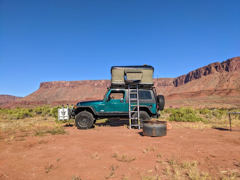 A Jeep with a rooftop tent setup in the scenic Castle Valley, Utah, under a clear blue sky.