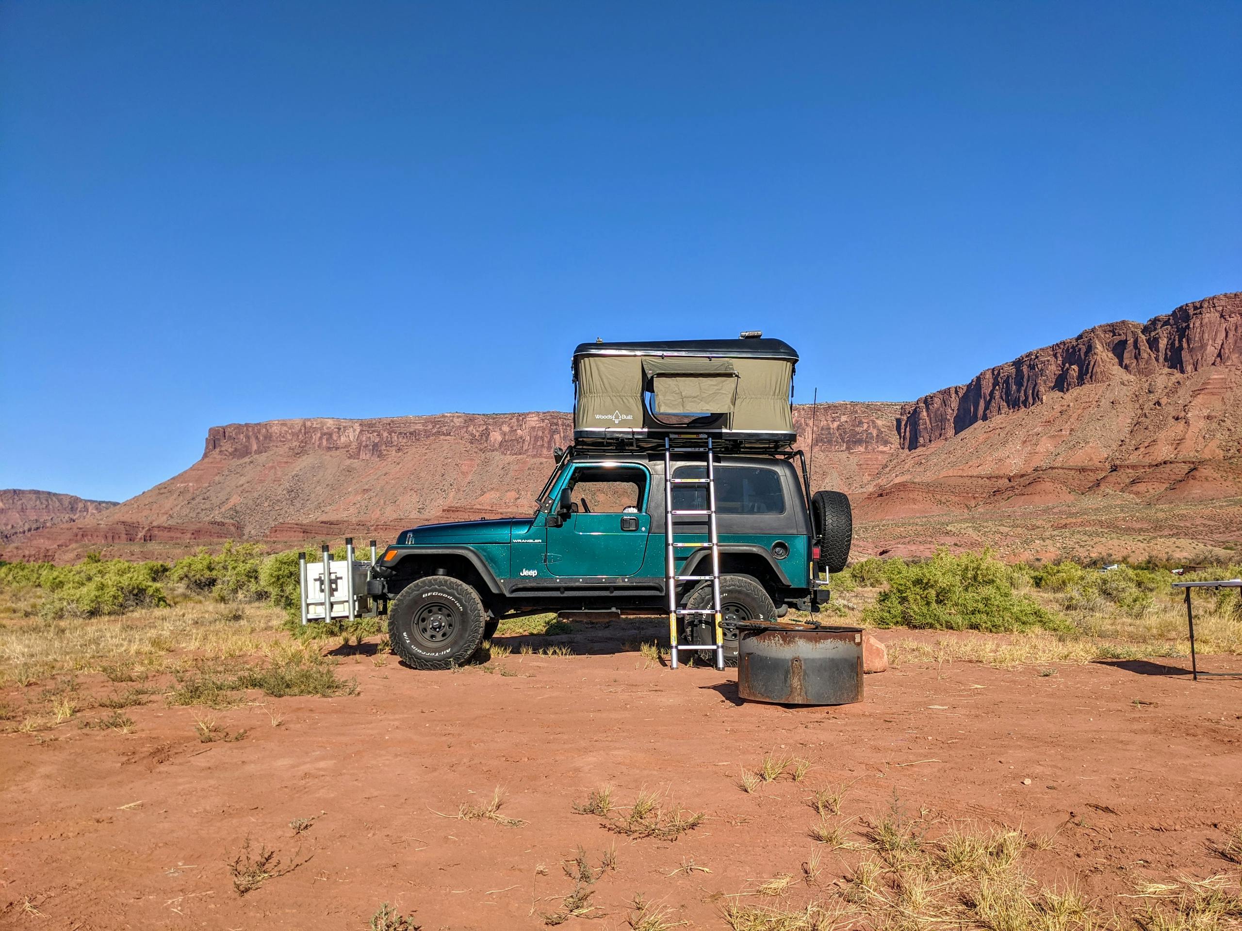 A Jeep with a rooftop tent setup in the scenic Castle Valley, Utah, under a clear blue sky.