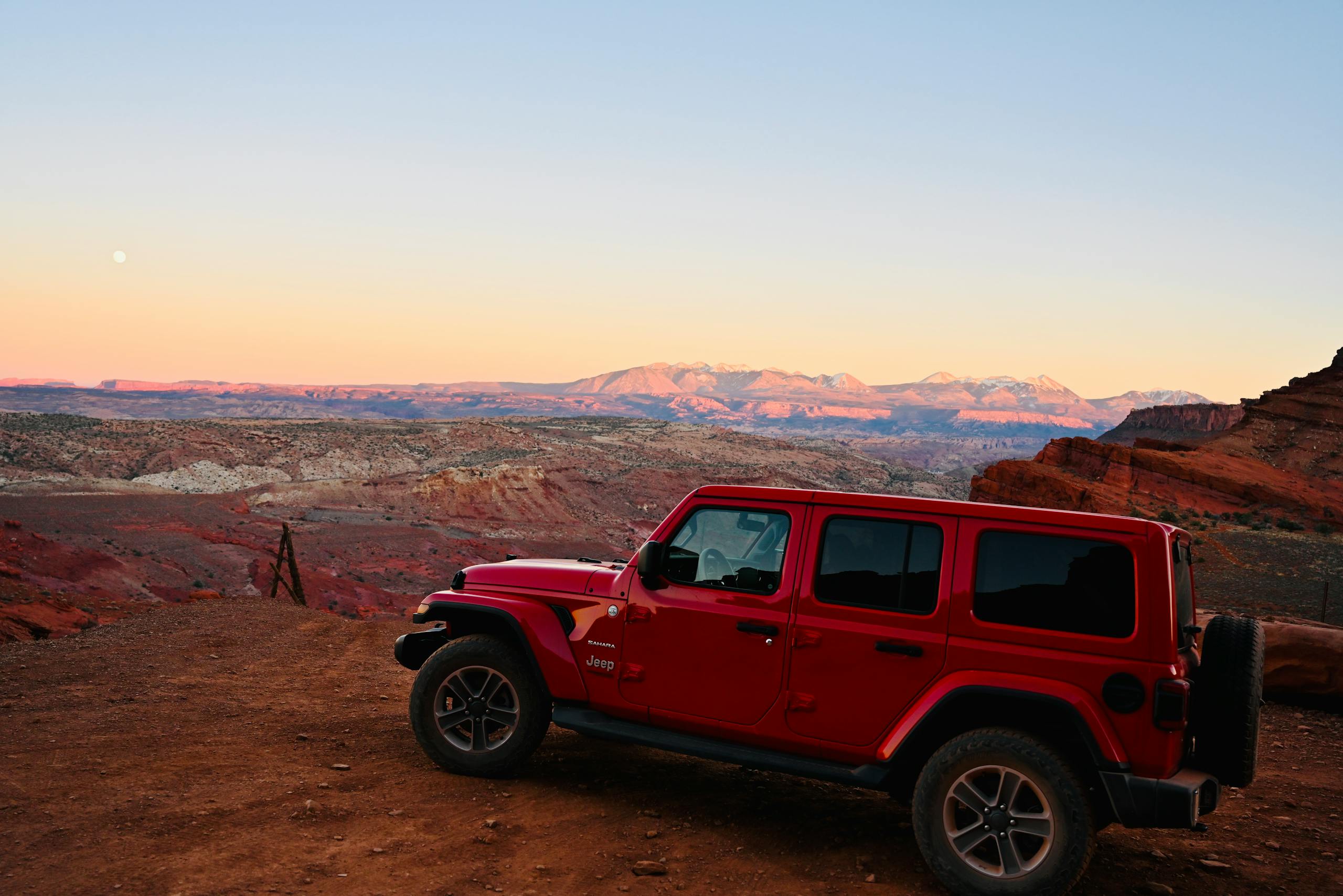 Red Jeep Wrangler at sunset in Moab, Utah, showcasing rugged outdoor adventure.