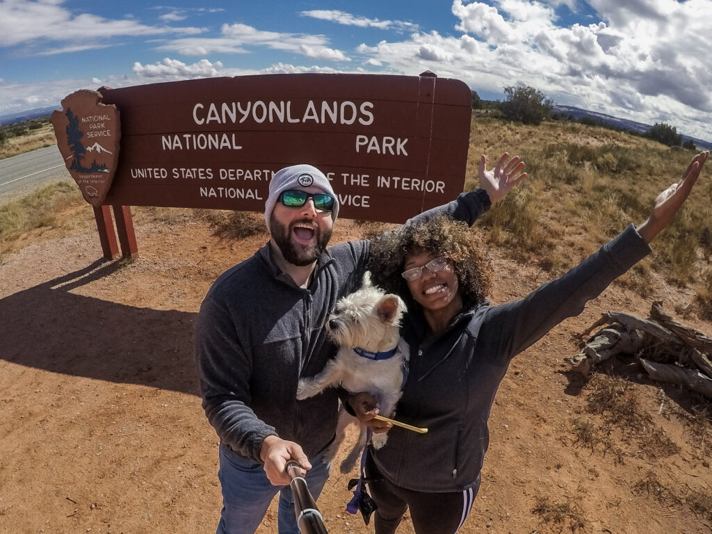 Rocio and Gabe with their dog Wilson stand in front of the canyonlands National Park sign entering Island In the Sky District