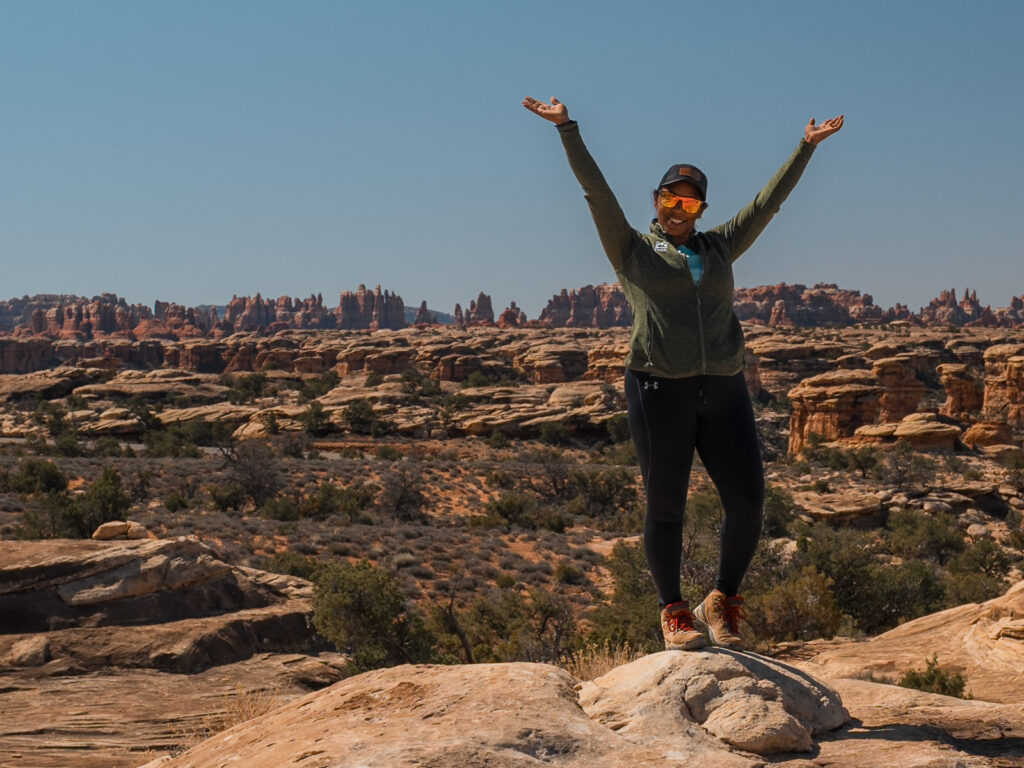 Rocio Standing hands up in Canyonlands National Park with The Needles District as a backdrop