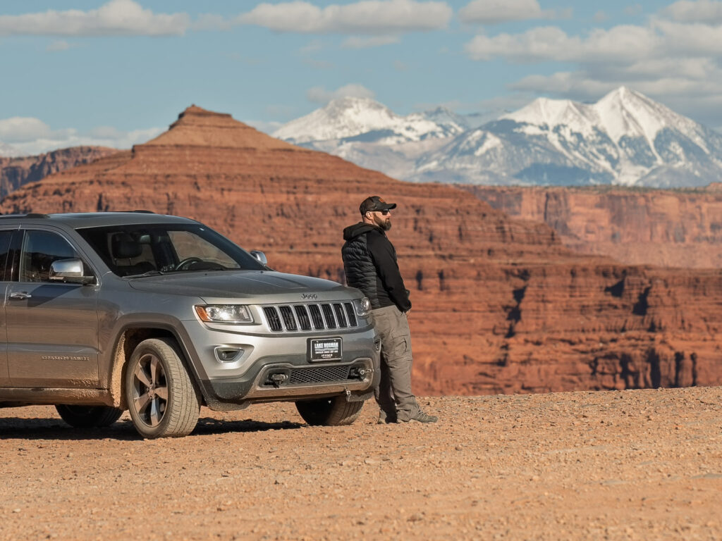 Gave in front of a gray jeep looking at the red rocks in dead horse point state park and snow covered La Sal mountains in winter near Moab Utah