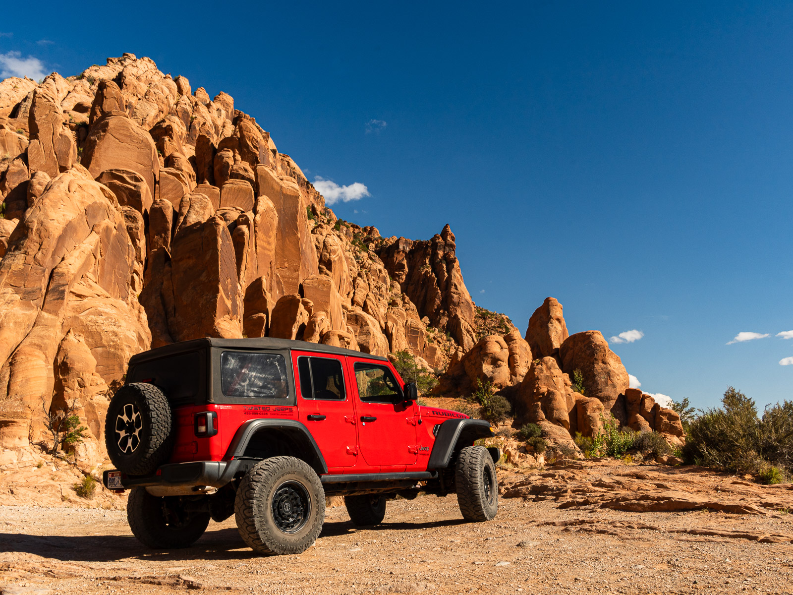 A red jeep wrangler parked in front of a red rock mountain in Moab, Utah.