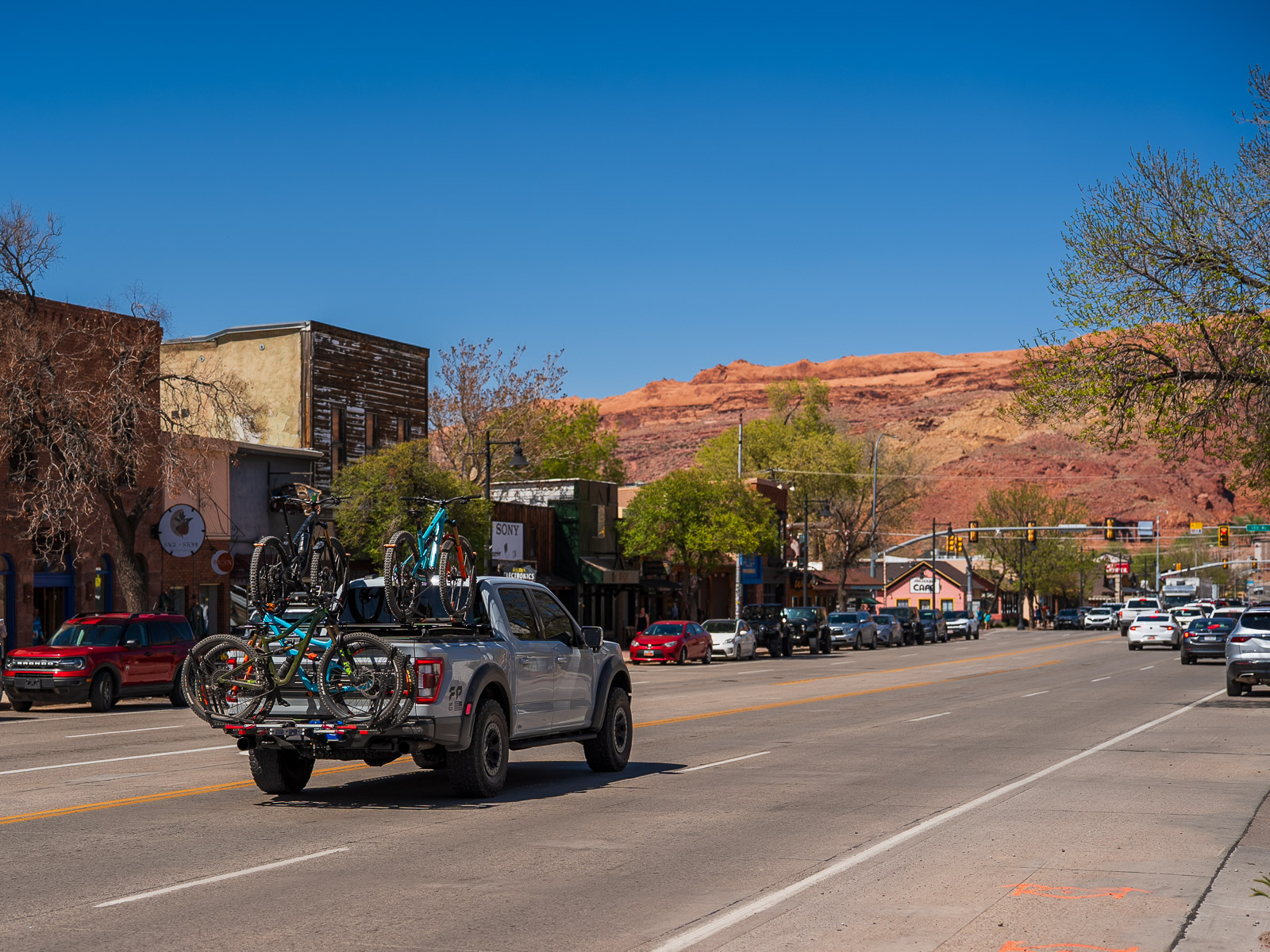 Pick up truck with bikes on the truck bed and more on the bumper while driving through the middle of town in Moab Utah Highway 191.