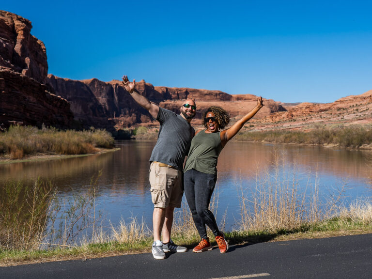 Rocio and gabe happy with their hands up in front of the Colorado river and red rock formations in Moab Utah
