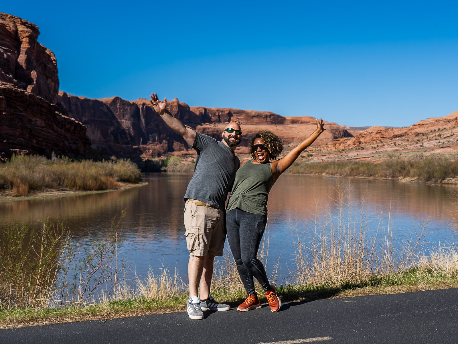 Rocio and gabe happy with their hands up in front of the Colorado river and red rock formations in Moab Utah