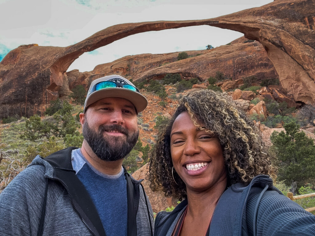 Rocio and gabe smiling in front of landscape arch in arches national park