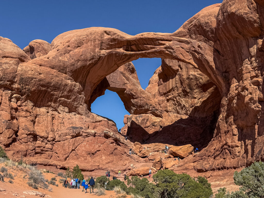 People walking towards Double Arch in Arches National Park, showing the scale of the sandstone formation.